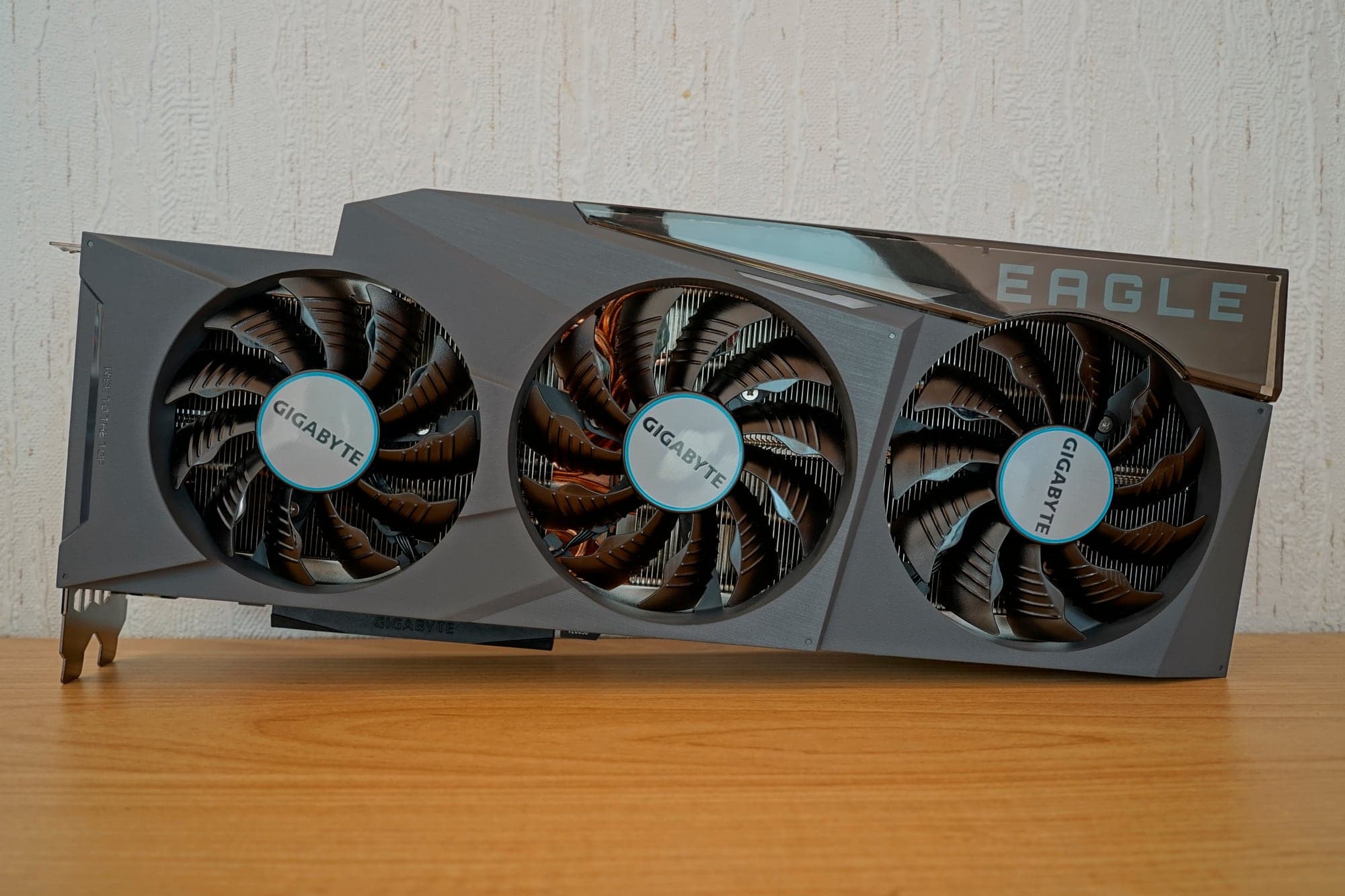Carte graphique Gigabyte GeForce RTX 3090 Eagle OC à trois ventilateurs, posée de face sur une table en bois devant un mur blanc