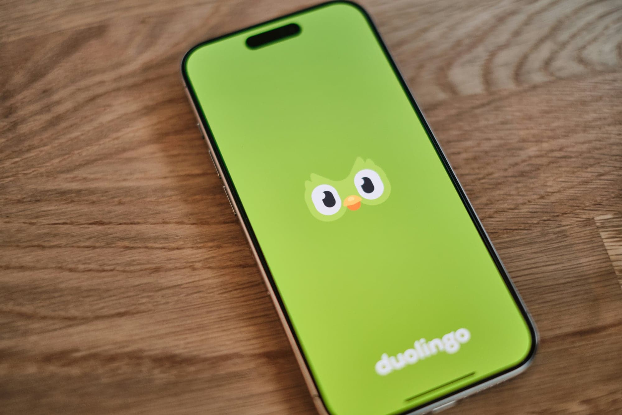 Smartphone posé sur une table en bois, écran vert affichant la chouette mascotte et le logo de l'application d'apprentissage des langues Duolingo