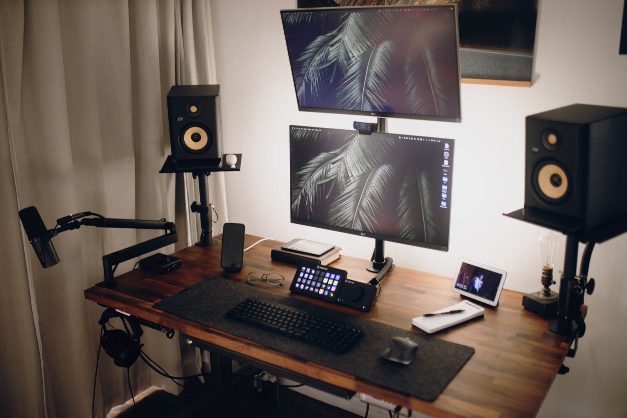Poste de streaming inoccupé sur un bureau en bois : micro sur bras articulé, deux écrans superposés avec une webcam fixée entre eux, enceintes de monitoring, clavier et pupitre de commandes à touches lumineuses.