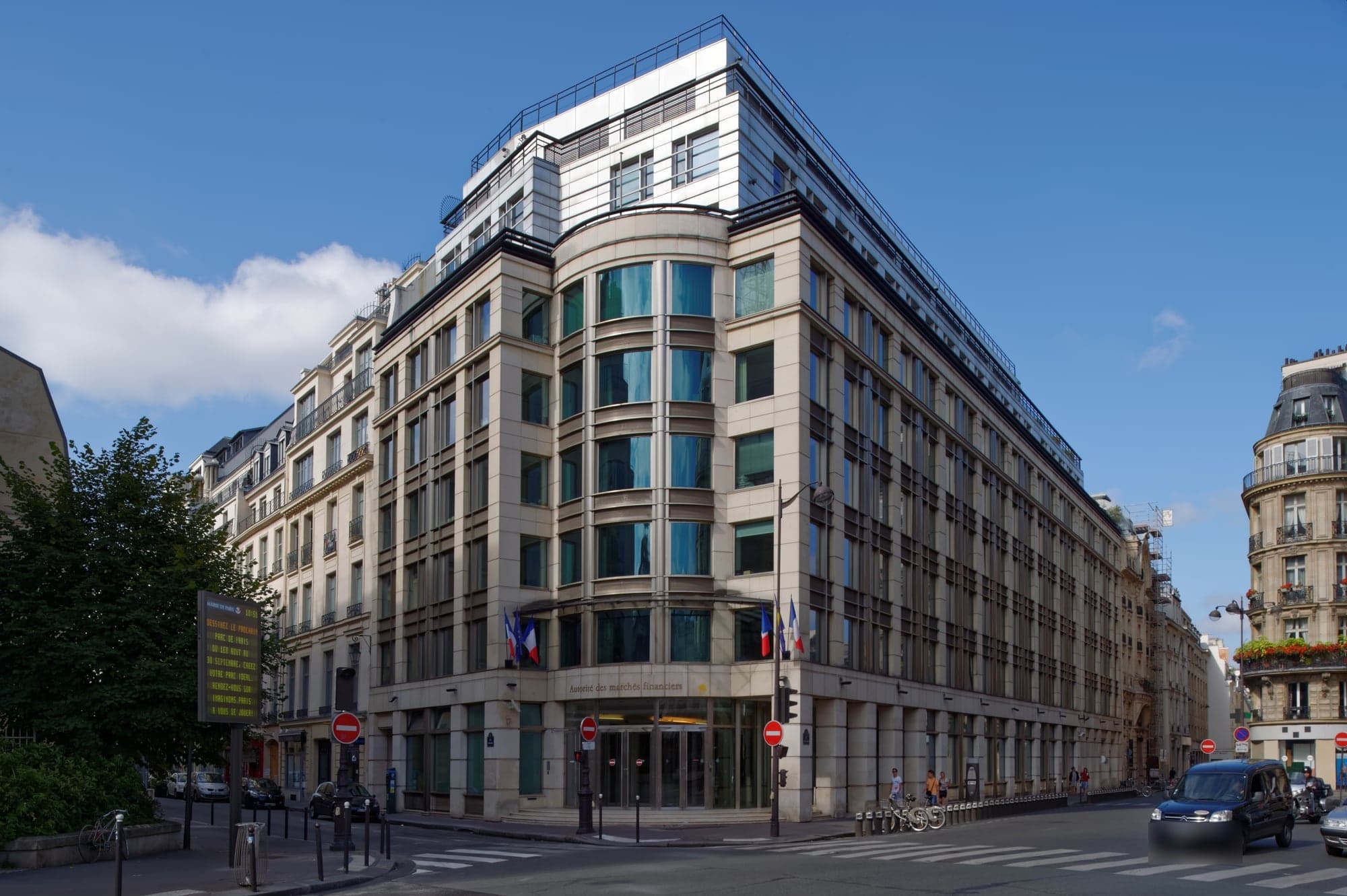 Immeuble d'angle en pierre claire et en verre, pavoisé de drapeaux français et européens, qui abrite le siège de l'Autorité des marchés financiers, place de la Bourse à Paris, sous un ciel bleu