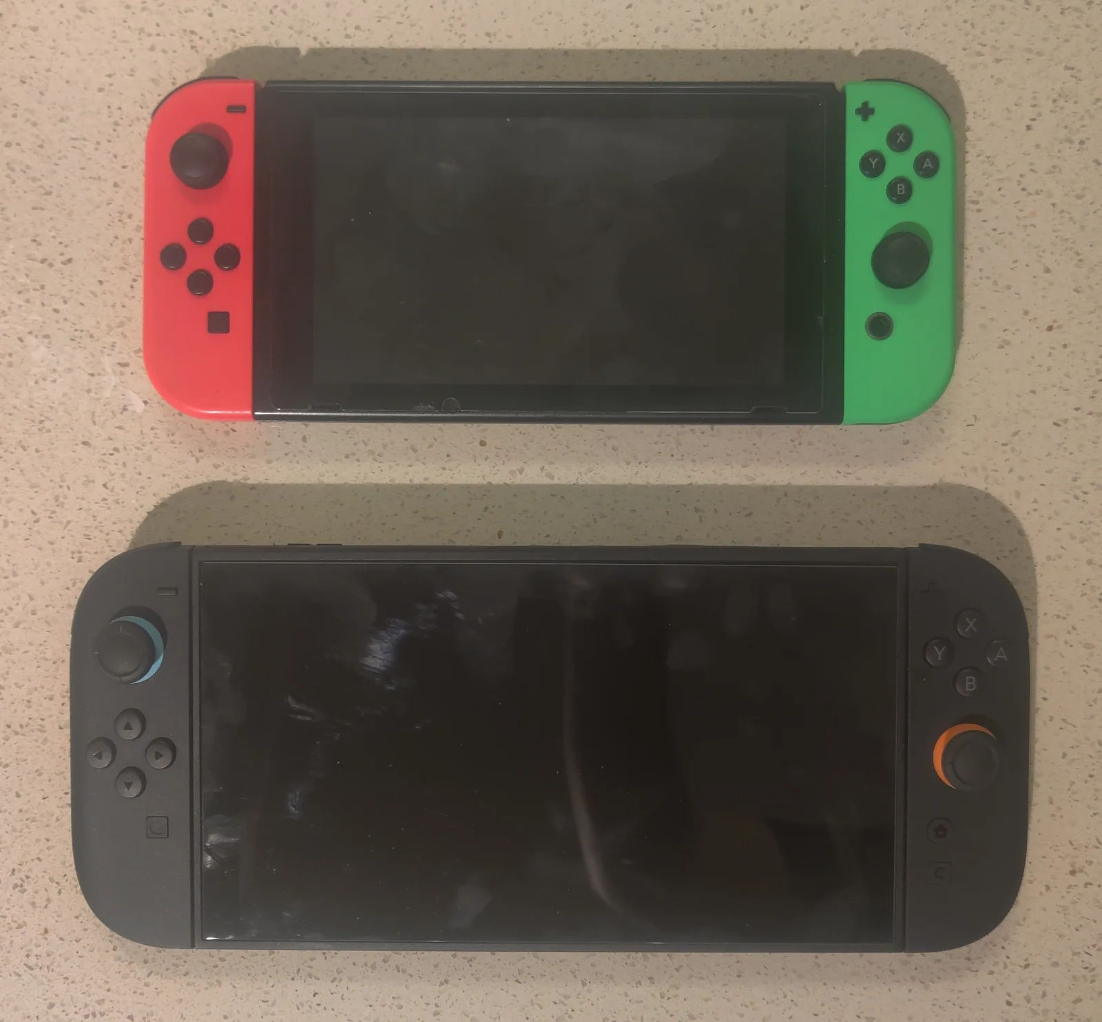 Une Nintendo Switch d'origine aux Joy-Con rouge et vert posée au-dessus d'une Switch 2 noire, nettement plus grande, dont les sticks sont cerclés de bleu et d'orange