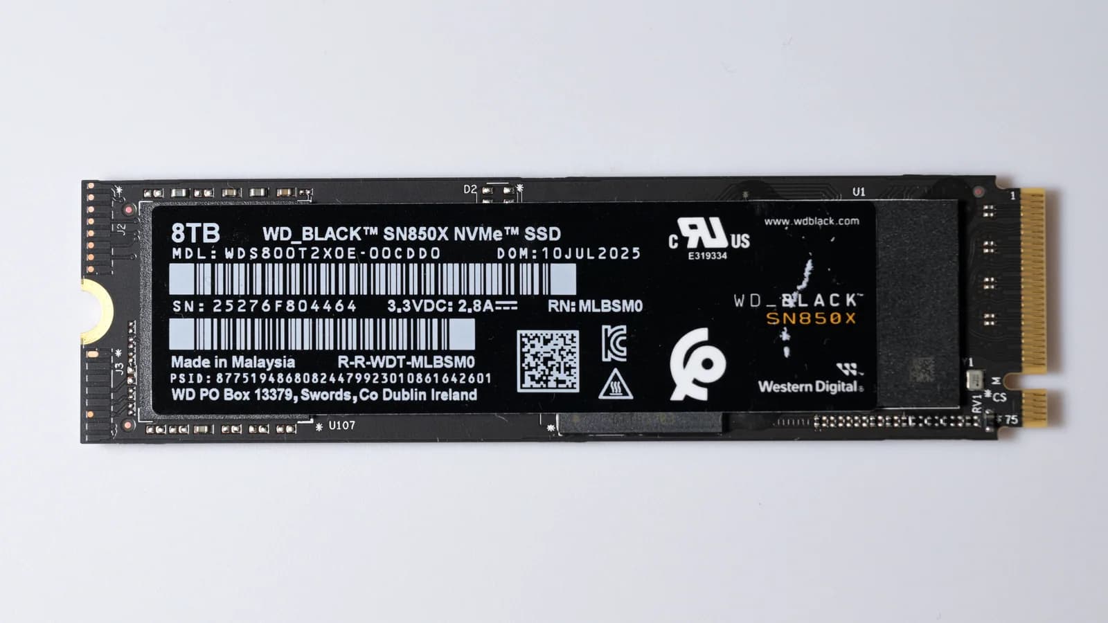 SSD NVMe Western Digital WD_Black SN850X de 8 To au format M.2 2280, une fine carte à étiquette noire photographiée sur fond gris clair